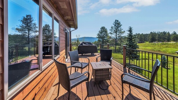 Een houten terras met buitenmeubilair, een barbecue en uitzicht op een groen landschap en bergen.