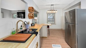 Una cucina moderna con piano di lavoro in legno, elettrodomestici in acciaio inossidabile e un lampadario.