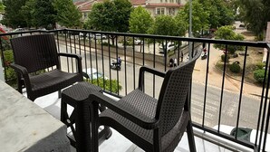 Un balcón con mobiliario de mimbre, vista a una calle y montañas al fondo.