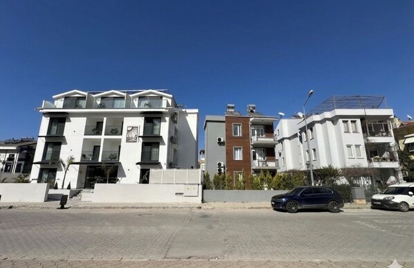 Un edificio residencial moderno con techo plano, varios balcones y entrada protegida por un portón.