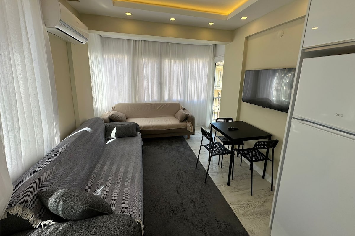 Uma sala de estar moderna com sofá, mesa de jantar com cadeiras, televisão de tela plana e aparelho de ar condicionado.