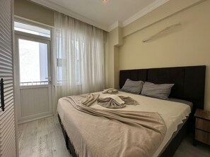 Un dormitorio con cama, una ventana con cortinas, una mesita de noche y una lámpara de pared.