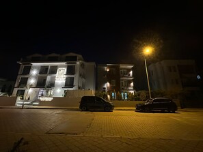 Un edificio de varios pisos con letreros iluminados, coches aparcados y una farola.