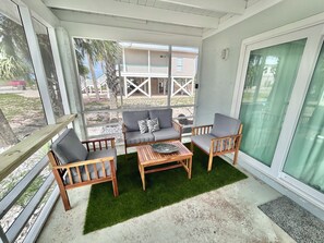A covered patio with a sofa, chairs, and a table. - Baked Beach Bungalow, across the street from the beach. (St. George Island)