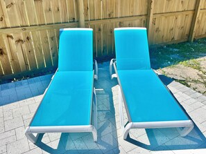 Two sun loungers with white frames and blue cushions, positioned on a tiled patio area. - Baked Beach Bungalow, across the street from the beach. (St. George Island)