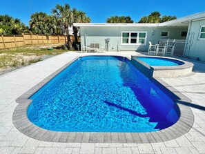 A rectangular swimming pool with a stone border, a smaller circular pool, and a house with a white exterior in the background. - Baked Beach Bungalow, across the street from the beach. (St. George Island)