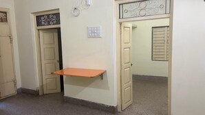 A hallway with a small orange shelf, a light switch, and a decorative metal grille above a door.