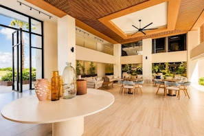 A spacious lobby with a high ceiling, large windows, and a central seating area with tables and chairs.