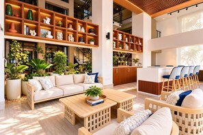 A modern living area with a sofa, coffee table, and chairs, a kitchen with a bar, and shelves with decorative items.