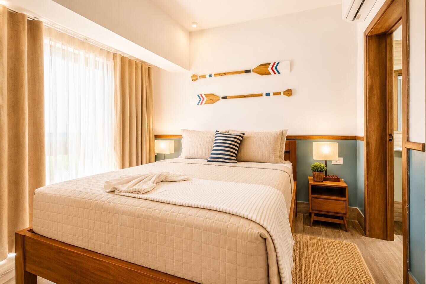 Habitación de hotel con cama, dos mesitas de noche con lámparas, un adorno en la pared y una puerta.