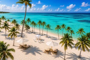 A beach with palm trees, white umbrellas, and lounge chairs. - Modern and Stylish  Condo in Exclusive Cap Cana, Perfect for a Relaxing Getaway (Punta Cana)