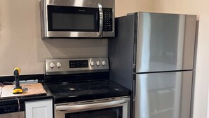 A compact kitchen with a stainless steel microwave, oven, and refrigerator.