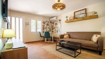 Een woonkamer met een bank, salontafel, lamp, en een eethoek met stoelen en een tafel.