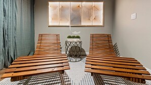 A room with two wooden benches, a small table with a plant, and a decorative window with a geometric pattern. - Walk to Lambeau, Titletown & Resch • Park 4 Cars • Sauna & Tailgate Garage (Green Bay)