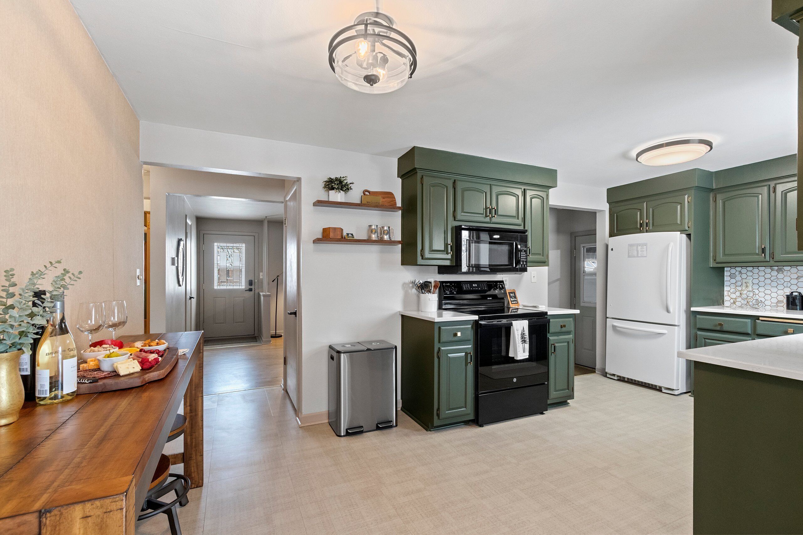 A modern kitchen with green cabinets, a stainless steel refrigerator, a microwave, and a stainless steel trash can.