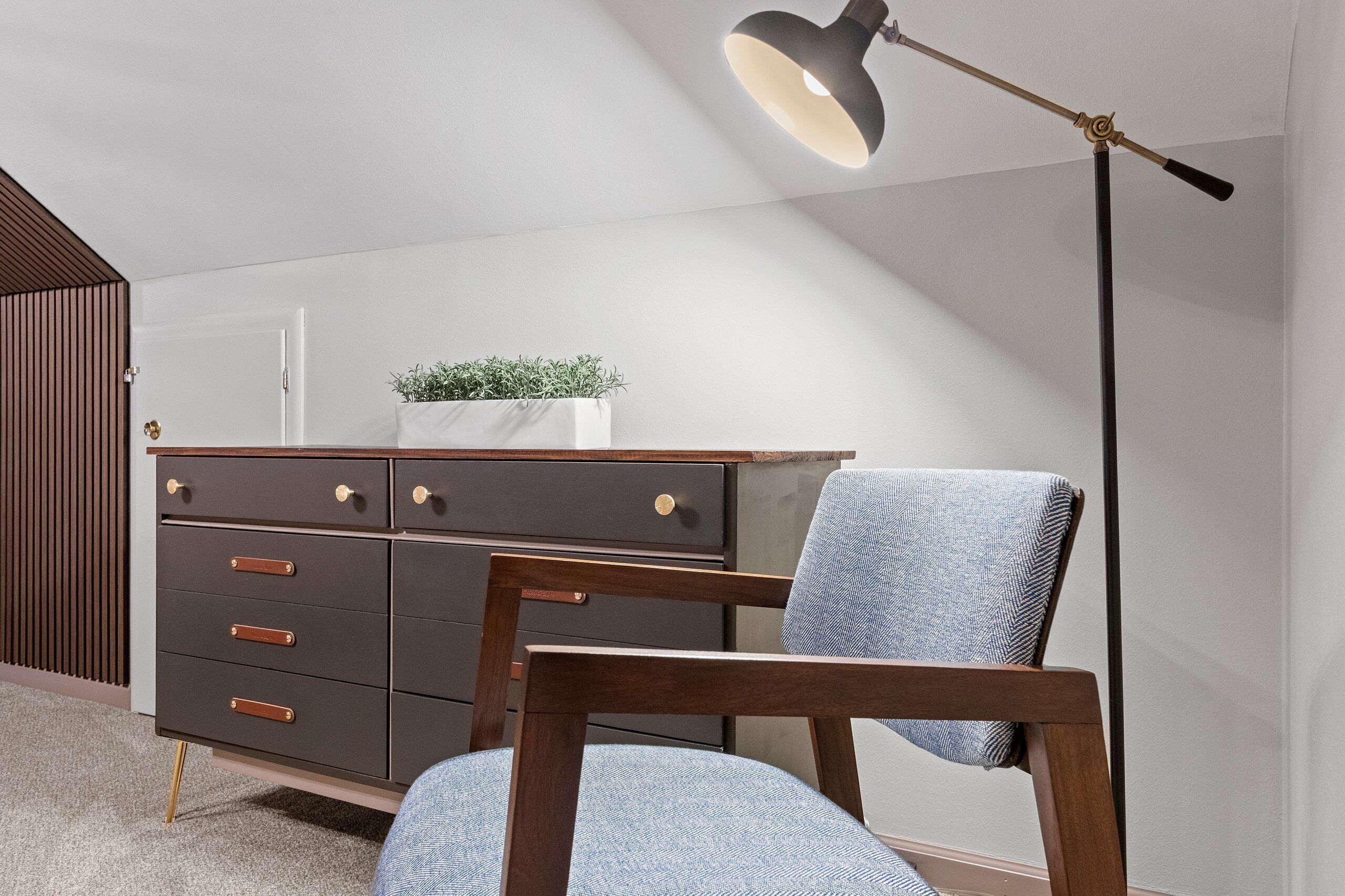 A modern room with a dark wooden dresser, a blue upholstered chair, and a floor lamp.