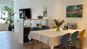 A modern dining area with a wooden floor, a white table with a floral tablecloth, and colorful chairs. - At the small mill pond - central quiet location with parking and bicycles (Flensburg)