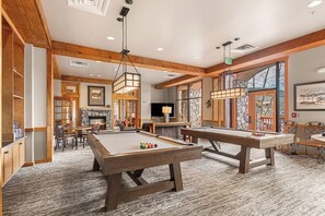 Ein geräumiger Raum mit Poolbillard, Kamin und großem Fenster mit Blick ins Freie.