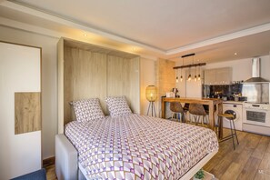 Ein modernes Schlafzimmer mit einem großen Bett, einem Holz-Kopfteil, einem Nachttisch und einer kleinen Küchenzeile mit Spüle und Herd.