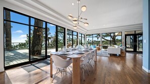 Un comedor moderno con una larga mesa preparada para seis comensales, ventanas amplias y una lámpara colgante.
