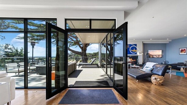Un interior moderno con una puerta de vidrio que da a un patio exterior, un sofá y un televisor.