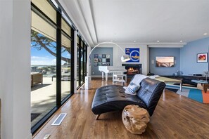 A modern living room with a large window, a fireplace, and a piano. - 4011 Big Little Lies - Modern, Oceanfront Home (Carmel)