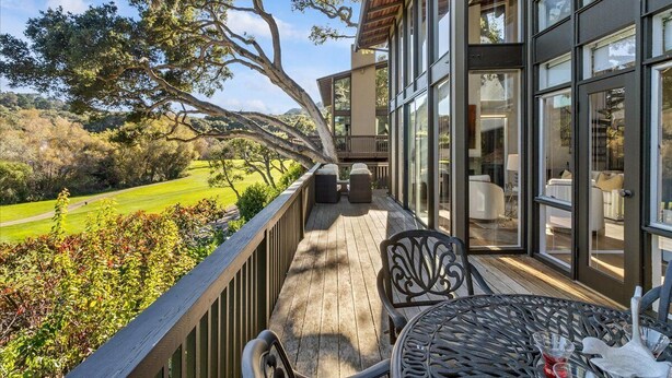Un balcon avec coin salon extérieur, une vue sur un terrain de golf et un bâtiment moderne doté de grandes fenêtres.