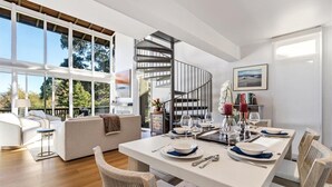 Un intérieur moderne comprenant un coin repas, un escalier en colimaçon et de grandes fenêtres.