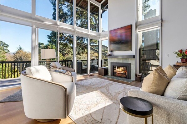 A modern living room with a fireplace, large windows, and a view of the outdoors.
