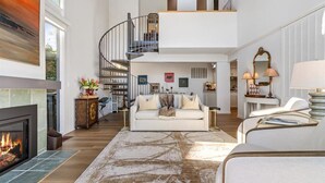 Un vaste espace de vie doté d’une cheminée, d’un canapé blanc, d’un escalier et d’un coin repas.