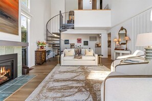 A spacious living area with a fireplace, a white sofa, a staircase, and a dining area.