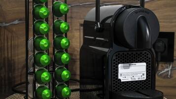 Een Nespresso koffieapparaat met een groene fleshouder ernaast.