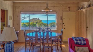 Un coin repas avec une table et des chaises, une fenêtre donnant sur un paysage agréable et une croix accrochée au mur.
