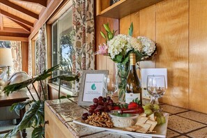 A table with a wine bottle, glasses, grapes, nuts, and crackers, with a framed welcome sign and a floral arrangement. - 4045 Mission Hill ~ Mission Ranch, Point Lobos View (Carmel)