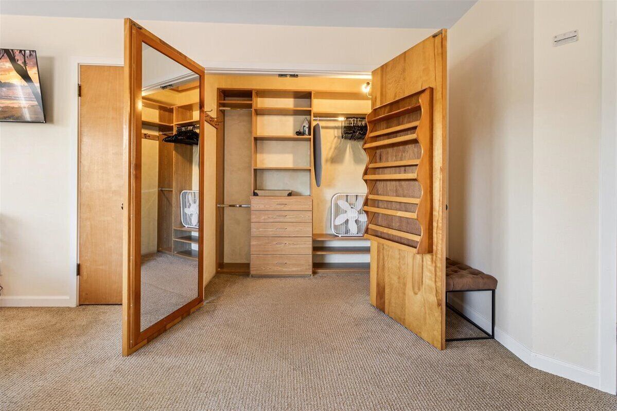 A walk-in closet with open doors, shelves, and a bench.