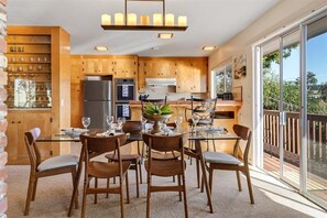 A modern kitchen with wooden cabinets, a central island, and a dining area with chairs and a table. - 4045 Mission Hill ~ Mission Ranch, Point Lobos View (Carmel)
