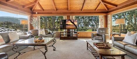 A covered outdoor seating area with leather sofas, a wooden coffee table, and a view of the surrounding landscape.