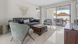 A modern living room with a leather sofa, a grey armchair, a wooden coffee table, and a glass door leading to an outdoor patio. - Spacious 4-bed House With Secure Parking (Brisbane)
