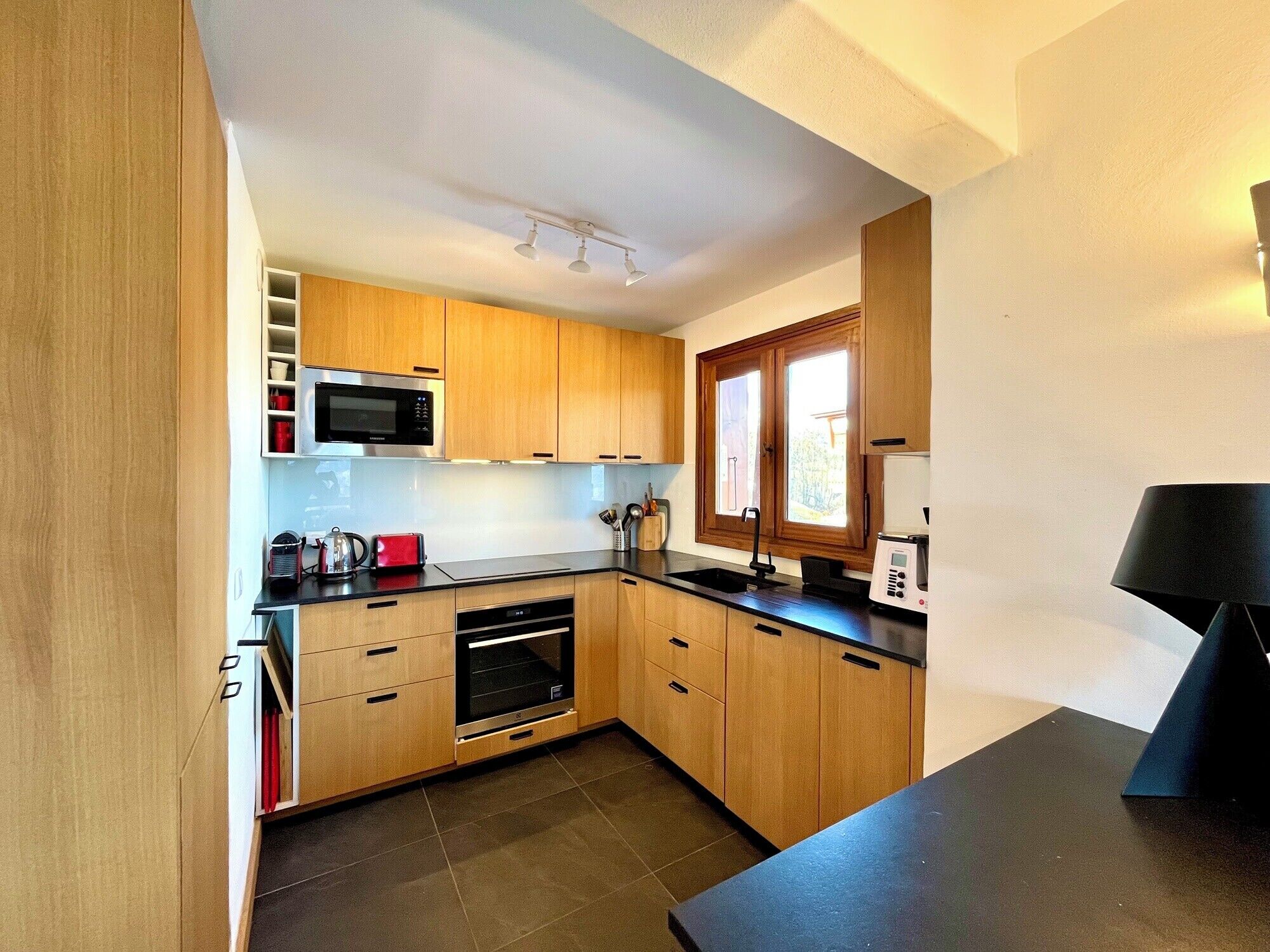 A compact kitchen with wooden cabinets, a microwave, a toaster, and a sink.