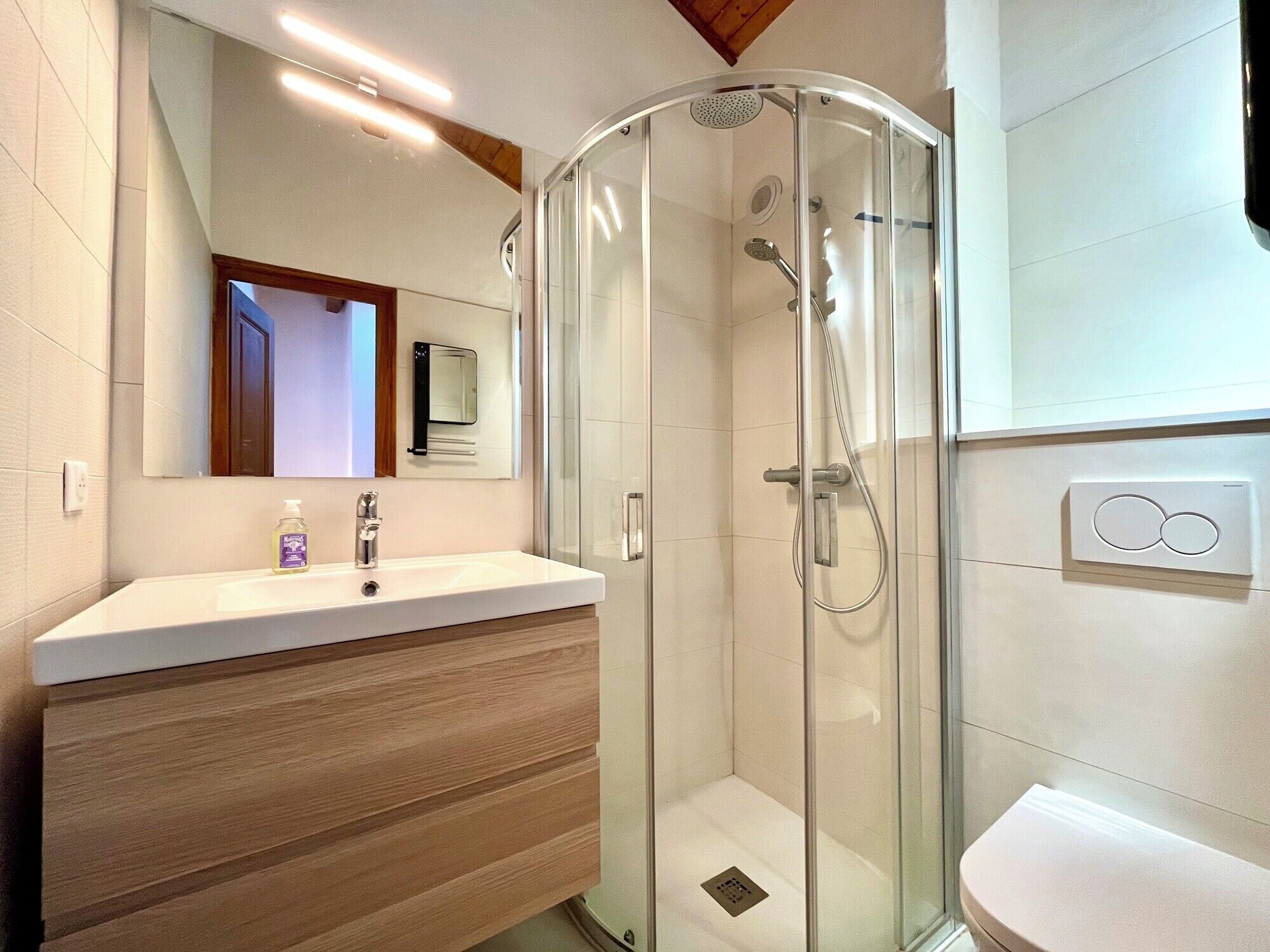A modern bathroom with a glass-enclosed shower, a wooden vanity, and a white sink.