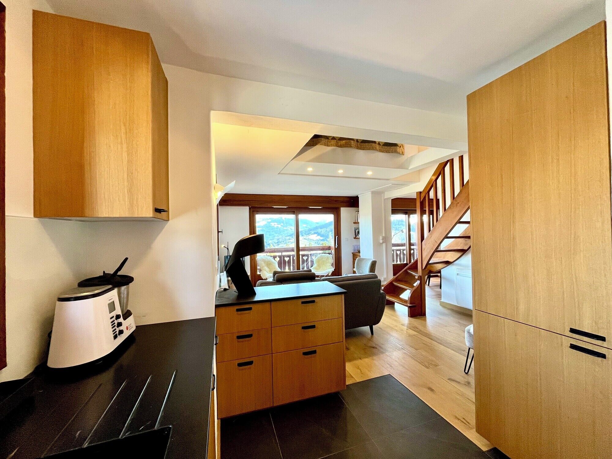 A modern kitchen with wooden cabinets, a coffee maker, and a dining area with a sofa and a staircase.
