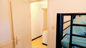 Quarto de hotel com uma cama, uma porta, um radiador e um corredor que leva a outro quarto.