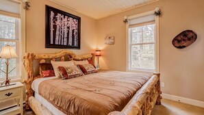 A bedroom with a large bed, wooden headboard, a framed picture on the wall, and two windows. - New Listing! National Forest Access + Hot Tub | Continental Divide | Deck (Fairplay)