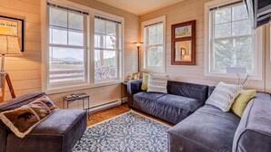A cozy living room with a large window, a dark leather sofa, a small table, and a patterned rug. - New Listing! National Forest Access + Hot Tub | Continental Divide | Deck (Fairplay)