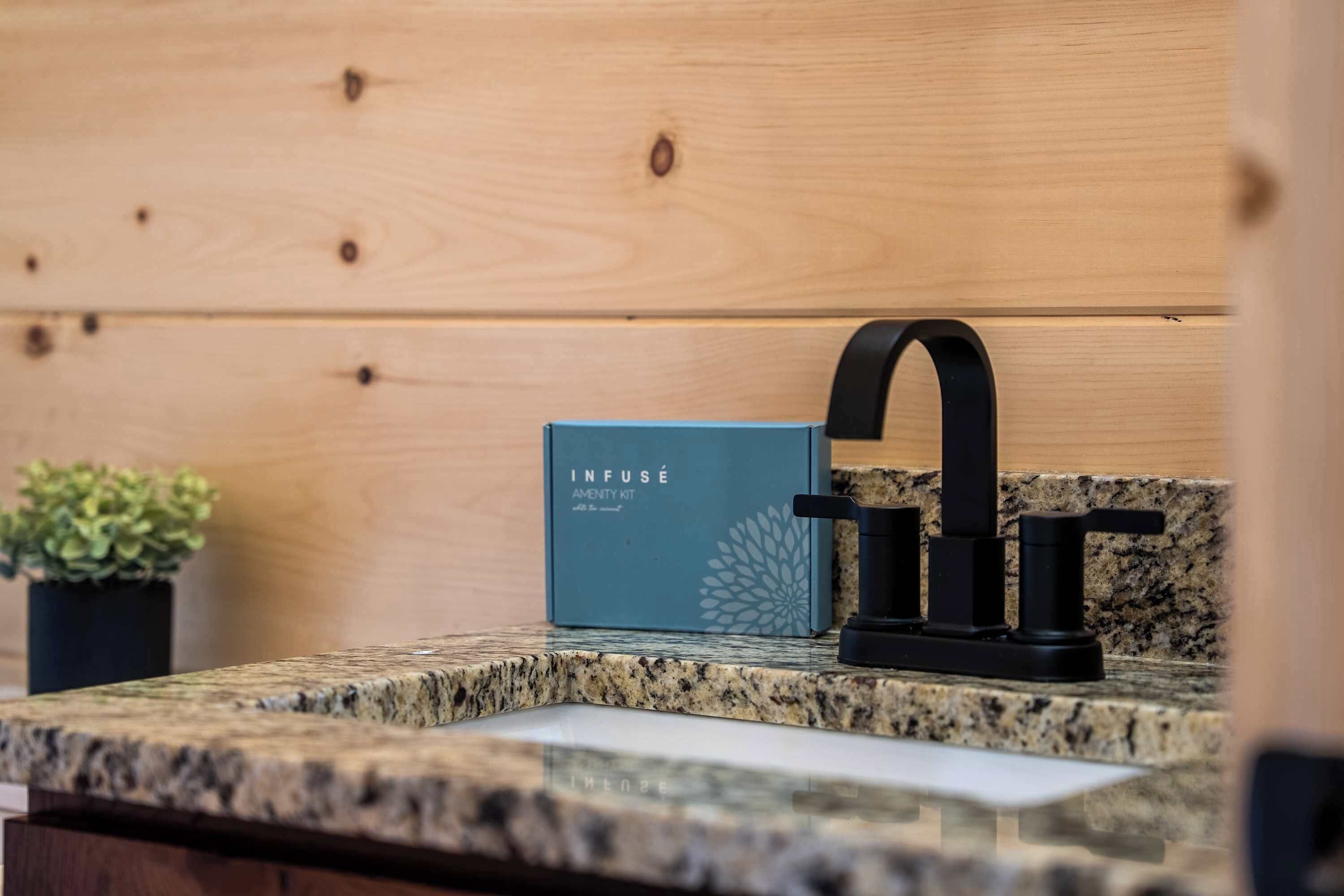 Een keuken met een granieten aanrecht, een zwarte kraan en een blauwe Infuse Amenity Kit doos.