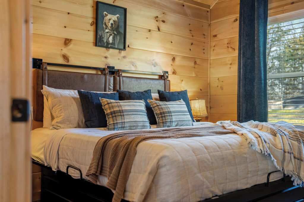 A wooden-paneled bedroom with a bed, pillows, and a framed picture on the wall.