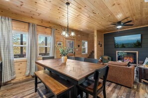 A wooden interior with a dining table, benches, a sofa, and a fireplace. - Modern Pigeon Forge Cabin | Hot Tub, Game Loft (Pigeon Forge)