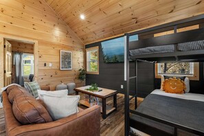 A cozy cabin interior with a wooden ceiling, a bunk bed, a sofa, and a small table with a plant. - Modern Pigeon Forge Cabin | Hot Tub, Game Loft (Pigeon Forge)