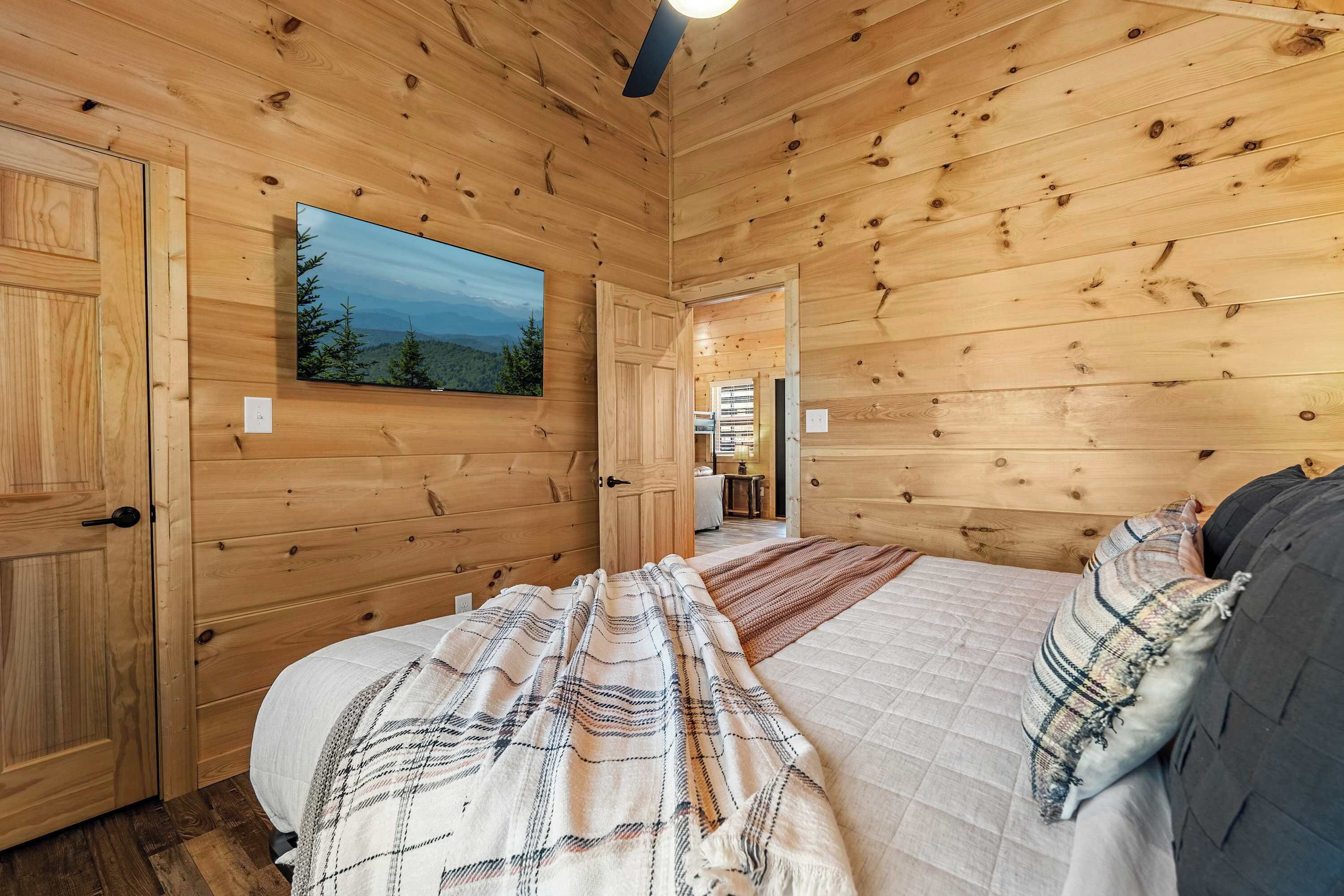A wooden cabin room with a bed, a large window with a view, and a door leading to another room.
