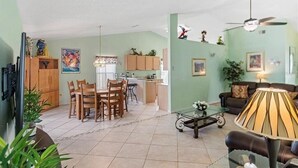 A spacious living area with a dining table, chairs, a sofa, and a coffee table. There is a kitchen area with cabinets and a refrigerator. - Summer 35% Off 4BR Pool Villa/Game Room (Kissimmee)